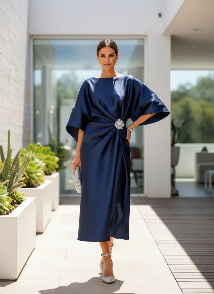 Woman in a navy blue dress standing on a modern patio with plants and a building in the background.