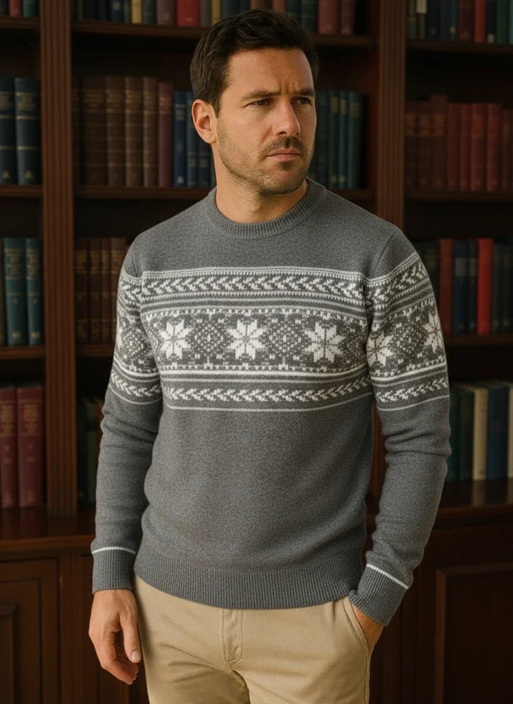Man wearing a gray sweater with white patterns in front of a bookshelf.
